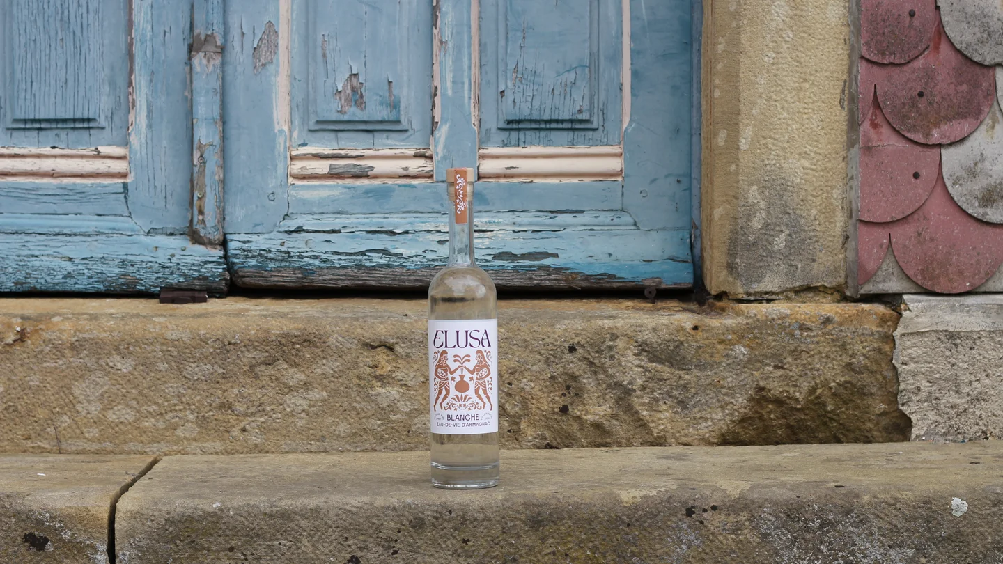 Elusa Blanche Armagnac bottle resting on the steps of a Gascon chateau