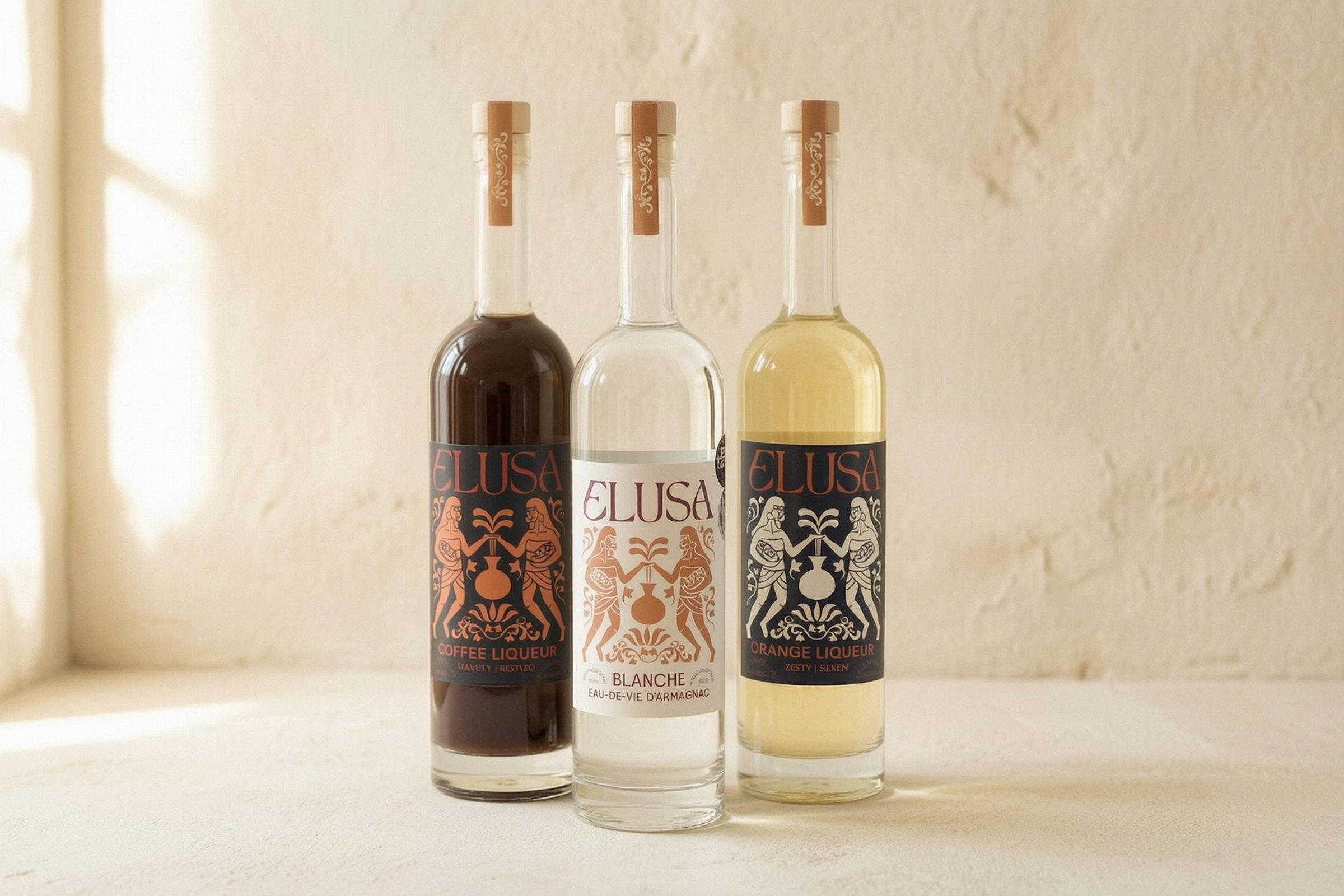 The Elusa collection — Coffee Liqueur, Blanche Armagnac, and Orange Liqueur bottles lit by soft natural light against a cream plaster wall