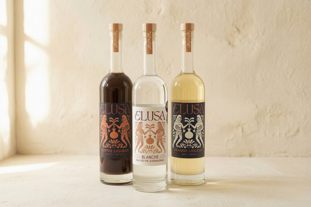The Elusa collection — Coffee Liqueur, Blanche Armagnac, and Orange Liqueur bottles lit by soft natural light against a cream plaster wall